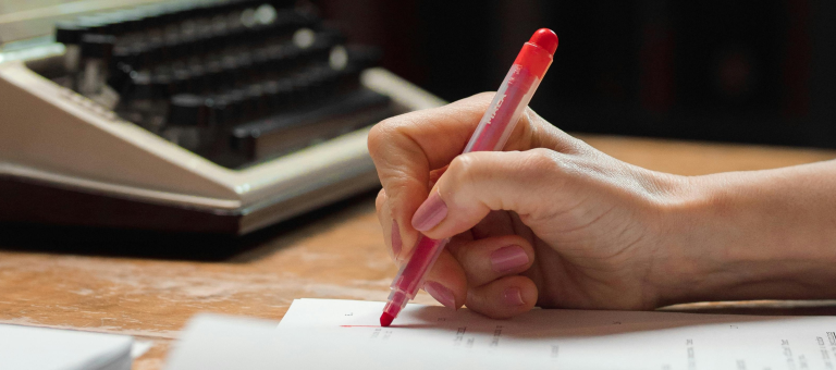 typewriter, hand marking paper with red pen